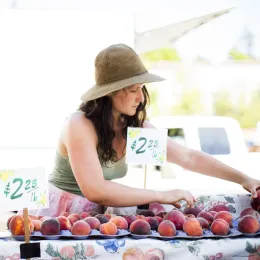 a farmer stands behind her peach stand