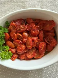 Roasted cherry tomatoes in a white bowl with a green garnish