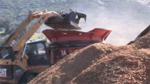 Photo of bucket tractor loading logs into tub grinder