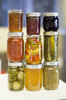 nine jars filled with various preserves, spreads, and pickled vegetables