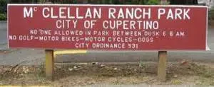 Wooden sign at McClellan Ranch Park entrance in Cupertino, with rules regarding park hours and usage restrictions.
