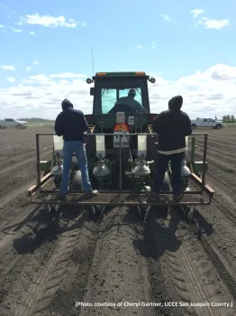 Tractor pulling a research planter with two people operating the planter.