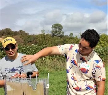 Dr. Sam Sandoval has students pouring water into the groundwater simulator model.