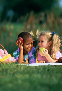 Two young children holding apples in a park