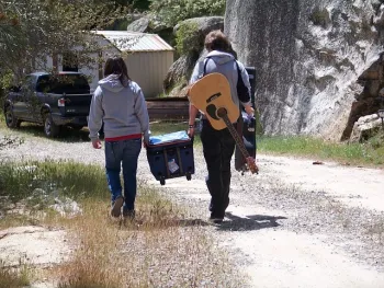 Couple walking in outdoor area with guitar and ice chest.