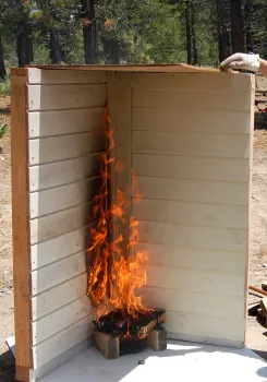 Fire started next to a home (to simulate flammable vegetation) penetrates combustible siding on a home component.