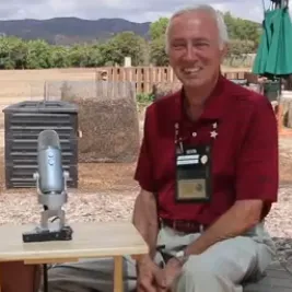 Tom Farrell sitting in front of a garden on a stool next to a table with a microphone.