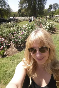 A headshot image of Michele Willer-Allread in the garden with roses in bloom behind her.