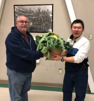 Master Gardener hands instructor gift basket with kale, cauliflower, and other vegetables.