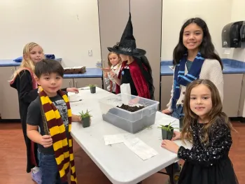 Smiling children gathered around a table using pots, plants, and soils for the activity.