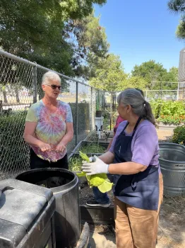 Two people standing next to a compost bin.