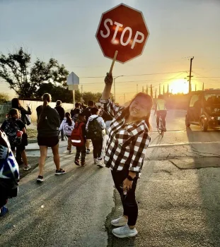 A woman holds a stop sign in a crosswalk as people walk and bike by