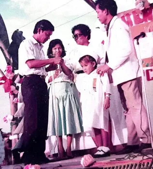 A girl poses with a graduation cap during a ceremony as adults stand around her