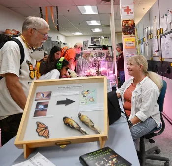 UC Davis alumnus John Whitehead, PhD, chats with UC Davis professor Elizabeth Crone. In the foreground is Noah Whiteman's book, 