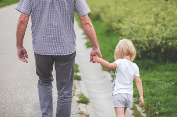 A person walking down a path holding a small child's hand.