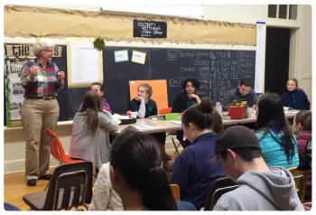 Youth sitting at tables with a 4-H adult volunteer addressing them