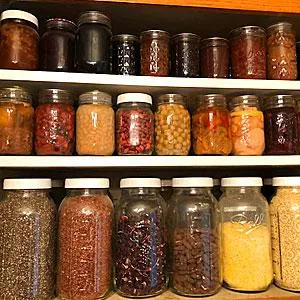 pantry shelf with three levels of items in jars including dried and canned beans. 
