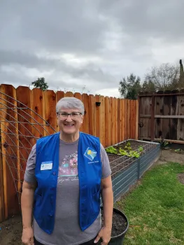 Master Gardener wearing blue vest, smiling in front of garden.