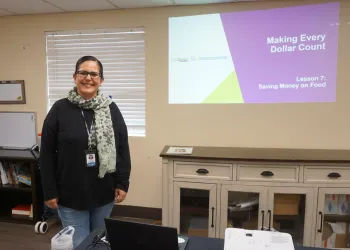 Maricarmen Anaya smiles next to the opening slide of Lesson 7 of her "Making Every Dollar Count" class
