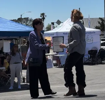 Chu, left, hands a certificate to Brauch outdoors with booths in background