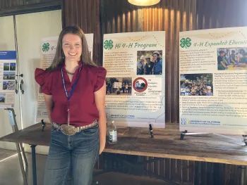 A young woman wearing a red top poses in front of 4-H posters