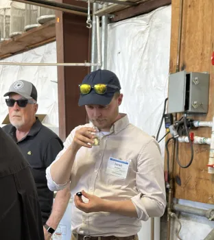 A man in a baseball cap sniffs a clear glass vial of liquid