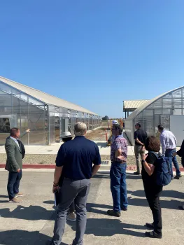 A man in a suit points to greenhouses under construction