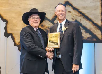 David Haviland, right, wearing a boutonniere made of wheat, receives a plaque from a man wearing a black cowboy hat