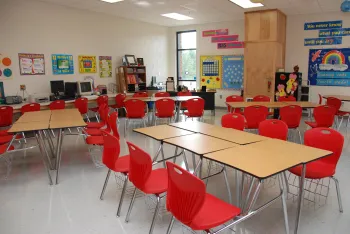 a classroom with red chairs, a table and posters on the walls