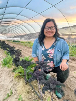 Lilian poses in a greenhouse next to a row of plants