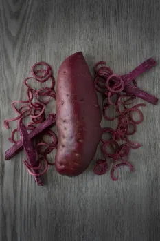 A whole dark purple-skinned sweetpotato flanked by pieces of purple sweetpotato flesh cut into curls