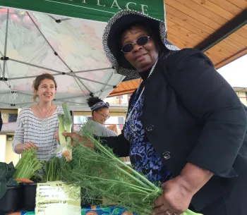Mary Blackburn holds green produce at a produce stand as a woman looks on