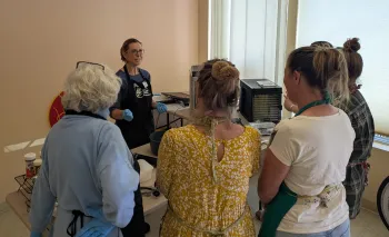 A group of adult watching another adult demonstrating jerky making.