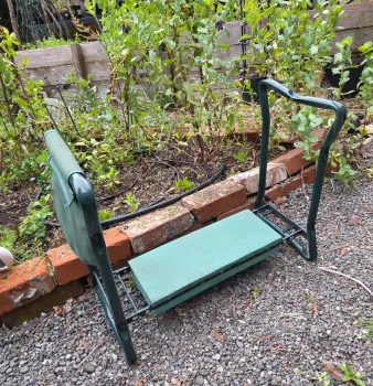 Green garden kneeler with padded seat next to a raised garden bed