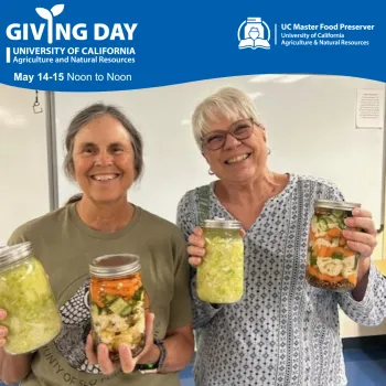 Photo of two people smiling while holding up jars of pickled vegetables. Text that reads "Giving Day May 14 to 15 from noon to noon".