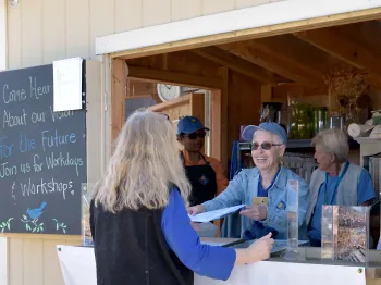 A smiling Master Gardener is handing information over a counter to someone