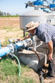 a farmer bends over inspecting his pump