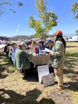 Participants gather around a shaded outdoor table during a garden journaling workshop at the Native Plant Boot Camp, listening as the instructor speaks.
