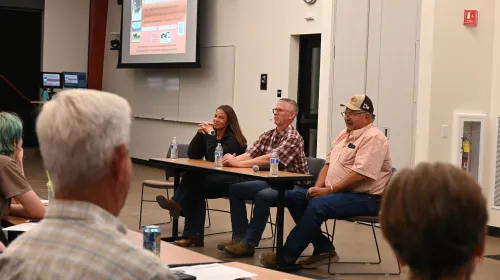 A woman and two men sit at a table facing an audience
