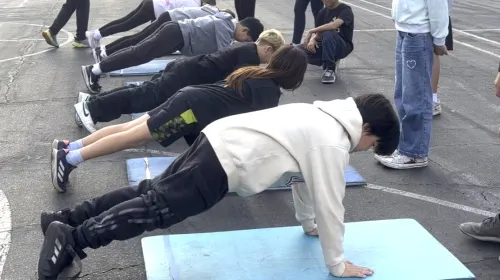 Six fifth-grade students do push ups at a school yard as part of fitness testing, while their peers look on
