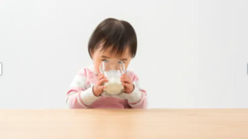 Small child wearing pink outfit holding glass with two hands drinking milk