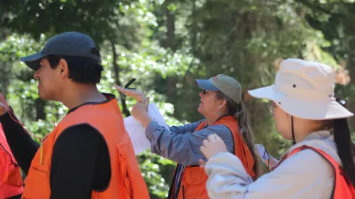 Group of people in orange vests use a compass.