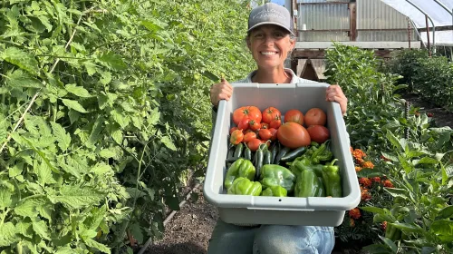 Leah Larsen of Bidwell Canyon Farm displays a container with a harvest of tomatoes and peppers from her hoophouse