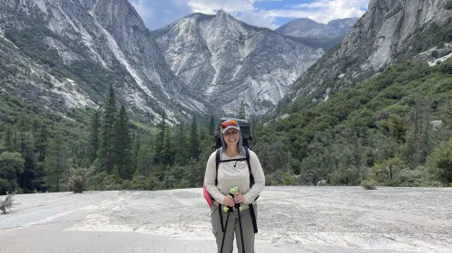 Kristin Polidoro stands with hiking poles, with Kings Canyon behind her and the South Fork of the Kings River below, unseen