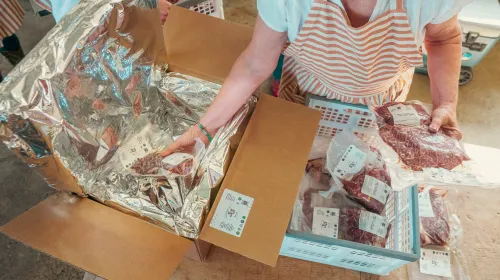 A person wearing an apron places vacuum-packed beef into a lined cardboard shipping box.