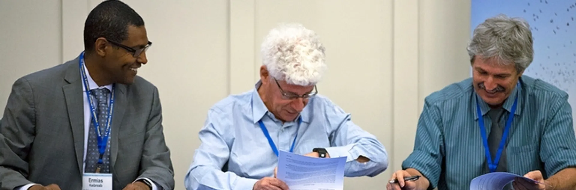 Three men sit at a table signing documents