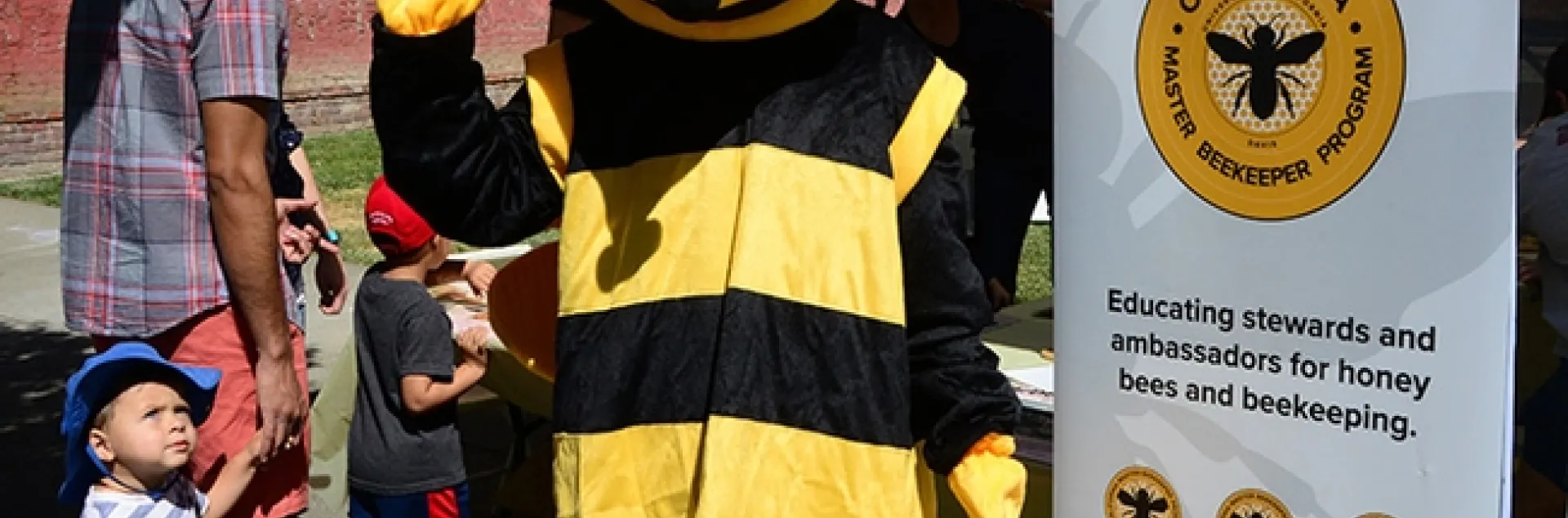 Wendy Mather, program manager of the California Master Beekeeper Program, stands in front of the booth at the California Honey Fstival while a youngster gives her a quizzical look. (Photo by Kathy Keatley Garvey)
