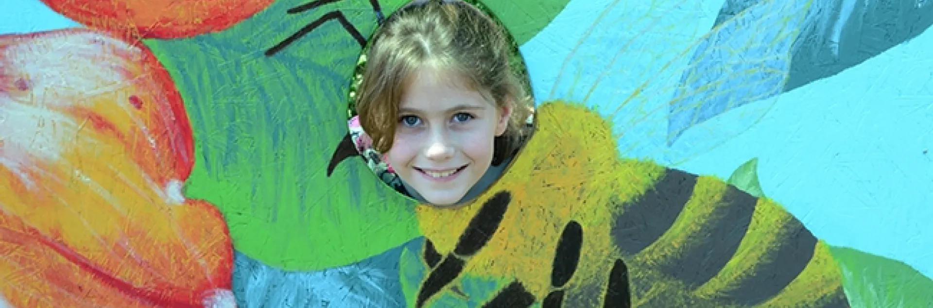 Beekeeper Adelaide Grandia smiles through a pollinator cut-out board. Her grandfather is teaching her beekeeping. (Photo by Kathy Keatley Garvey)
