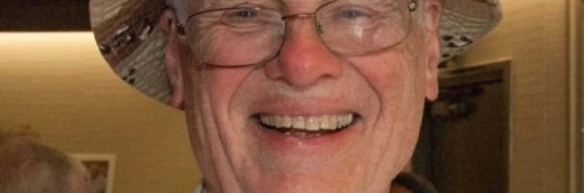 Headshot of Bill Leibhardt smiling, wearing striped, button-down shirt and a brimmed hat