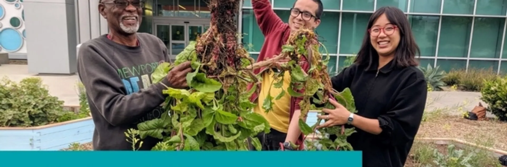 A diverse group of volunteers standing in front of the Long Beach Public Library holding a bunch of weeds.